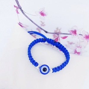 May include: A blue string bracelet with a blue and white evil eye charm.