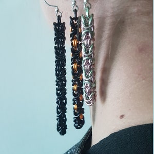 May include: Three long, dangling earrings with chain-like designs. The earrings are black, orange, and pink.