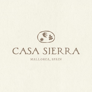 K&ouml;nnte beinhalten: Ein Logo auf einem strukturierten, cremefarbenen Hintergrund mit dem Text CASA SIERRA und MALLORCA, SPAIN in einer braunen Serifenschrift. &Uuml;ber dem Text befindet sich eine ovale Form mit einem handgezeichneten Vogel, einer Sonne und einer Pflanze.