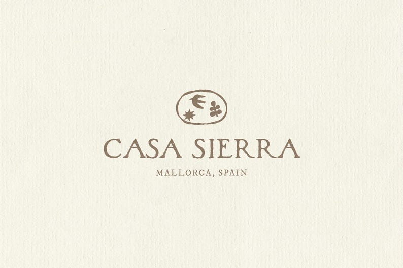 K&ouml;nnte beinhalten: Ein Logo auf einem strukturierten, cremefarbenen Hintergrund mit dem Text CASA SIERRA und MALLORCA, SPAIN in einer braunen Serifenschrift. &Uuml;ber dem Text befindet sich eine ovale Form mit einem handgezeichneten Vogel, einer Sonne und einer Pflanze.