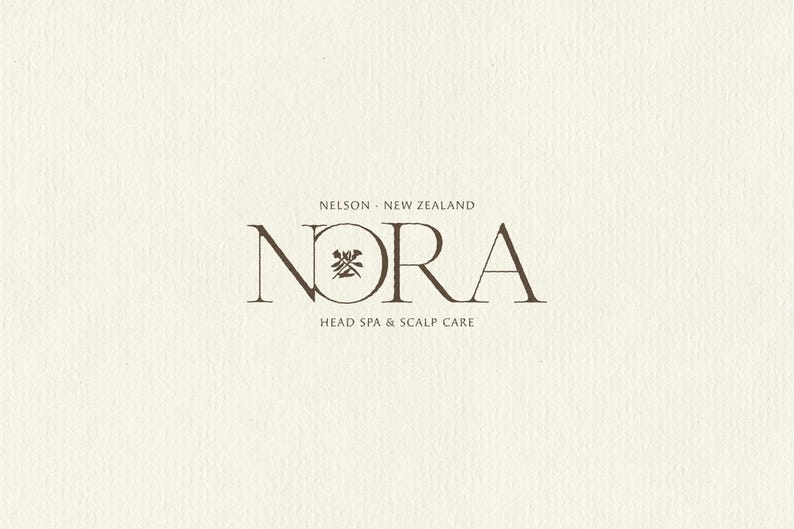 K&ouml;nnte beinhalten: Ein Logo-Design auf einem strukturierten cremefarbenen Hintergrund mit dem dunkelbraunen Schriftzug NORA in einer Serifenschrift. Der Buchstabe O enth&auml;lt ein kleines dunkelbraunes Grafiksymbol. &Uuml;ber dem Text steht NELSON NEW ZEALAND und darunter HEAD SPA & SCALP CARE.