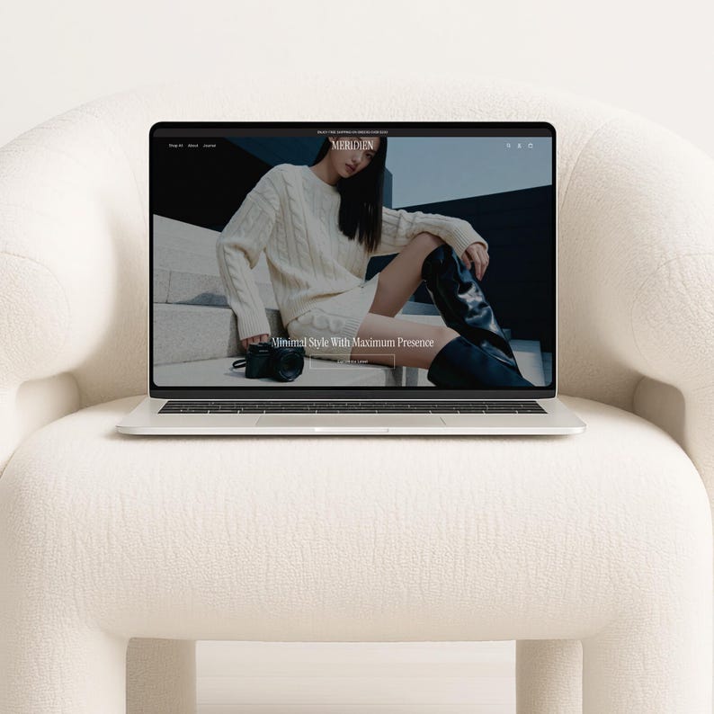 A laptop open to a fashion website homepage, resting on a textured white armchair.