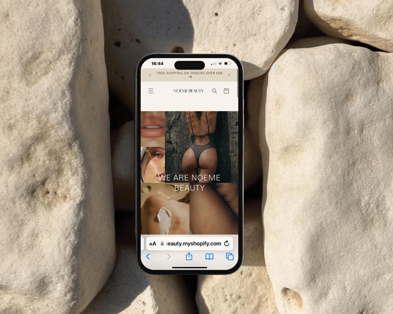 May include: A screenshot of a mobile phone displaying a website for a beauty brand called "Noeme Beauty". The website features a collage of images with the text "We are Noeme Beauty" and the website address "eauty.myshopify.com".
