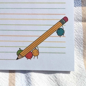 Puede incluir: Un bloc de notas blanco con líneas horizontales coloridas e ilustraciones de frutas y verduras. Un lápiz amarillo con una goma de borrar rosa está dibujado en la esquina inferior derecha. Siete estrellas amarillas en la parte superior. El bloc de notas está sobre una superficie a cuadros.