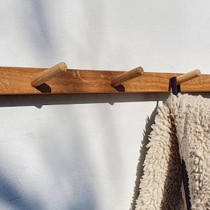 Peut inclure: Un porte-manteau mural en bois avec huit chevilles en bois. Une serviette moelleuse blanche est accrochée à l'une des chevilles.