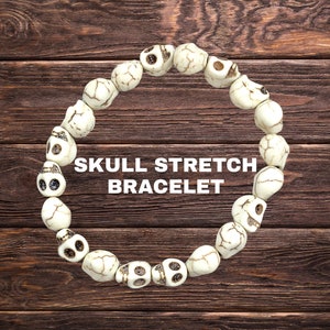 May include: A stretch bracelet composed of off-white skull beads. The beads have dark eye sockets and are strung together to form a circular shape. The text "SKULL STRETCH BRACELET" is displayed in white.