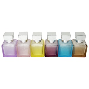 May include: Six small, square perfume bottles in a row, each with a different color of liquid inside. The bottles are lavender, pink, yellow, purple, blue, and brown. Each bottle has a silver square cap.