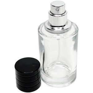 May include: A clear glass perfume bottle with a silver spray top and a separate black cap. The bottle is cylindrical and empty, with a visible spray tube inside. The cap is a solid black, stacked design.