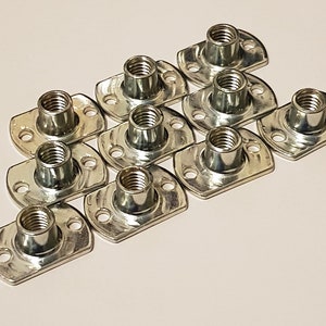 May include: A group of 10 silver-toned, flat-headed nuts with a square base. The nuts are arranged in a staggered pattern.