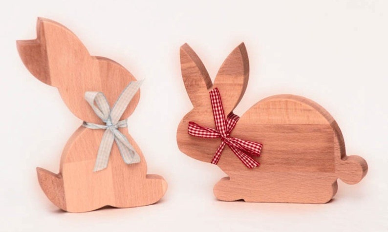 May include: Two wooden bunny shaped ornaments, one with a blue ribbon and the other with a red and white checkered ribbon.