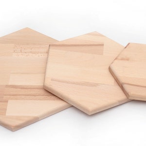 Puede incluir: Tres tablas de cortar hexagonales de madera de diferentes tamaños. Las tablas son de madera clara con un acabado natural.