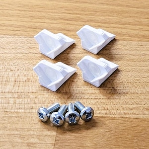 Op de afbeelding: Vier witte plastic kastdeurrubbers en vier zilveren schroeven zijn gerangschikt op een houten oppervlak. De bumpers zijn driehoekig met een cirkelvormige inkeping. De schroeven hebben een kruisvormige kop.