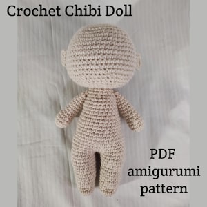 May include: A crocheted amigurumi doll in a light beige colour. The doll is a chibi style, meaning it has a large head and small body. The doll is standing on a white surface. The text "PDF amigurumi pattern" is visible in the bottom right corner of the image.