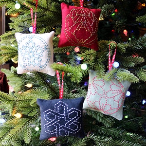 May include: Four handmade felt ornaments with snowflake designs in various colors, including red, white, blue, and green, hanging on a Christmas tree.