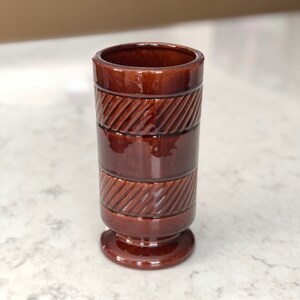 May include: A brown ceramic vase with a textured design. The vase has a wide base and a narrow opening.