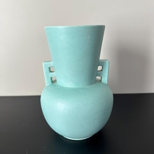 May include: A light blue ceramic vase with two handles. The vase has a rounded body and a narrow neck.
