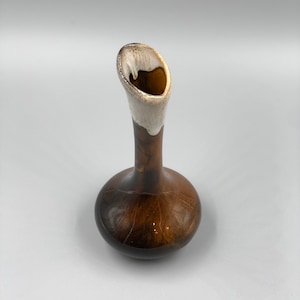 May include: A small, brown ceramic vase with a white glaze on the top. The vase has a rounded base and a narrow neck that flares out at the top.