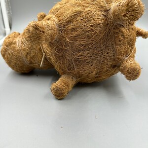 May include: A brown, handcrafted decorative hippo figurine made from natural fibers. The hippo has a rounded body, small ears, and stubby legs. The texture of the fibers gives the hippo a rustic, organic appearance. The figurine is lying on its side.