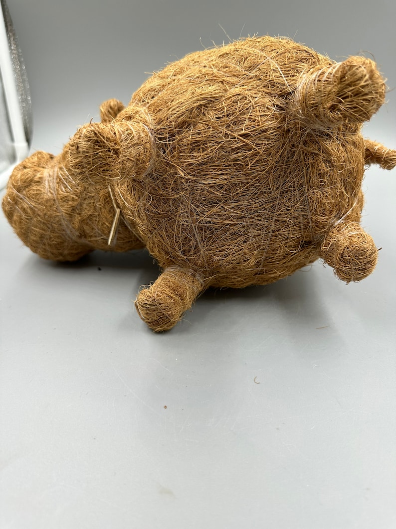 May include: A brown, handcrafted decorative hippo figurine made from natural fibers. The hippo has a rounded body, small ears, and stubby legs. The texture of the fibers gives the hippo a rustic, organic appearance. The figurine is lying on its side.