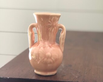 May include: A small, peach-colored ceramic vase with two handles and a floral design.