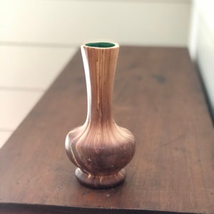 May include: A small wooden vase with a green top. The vase has a brown and light wood grain pattern.