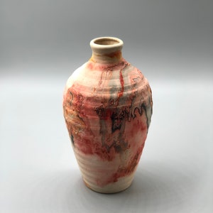 May include: A small, hand-thrown ceramic vase with a rounded body and a narrow neck. The vase is decorated with a colorful, abstract design in shades of pink, orange, and brown.