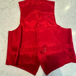 Puede incluir: Un chaleco rojo brillante hecho de un material brillante similar al sat&eacute;n. La parte trasera del chaleco es visible, mostrando una correa ajustable con una hebilla plateada. El chaleco tiene una forma cl&aacute;sica y a medida.