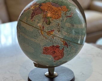 May include: A vintage globe with a blue and green map of the world. The globe is on a wooden stand and is in focus. The background is blurred.