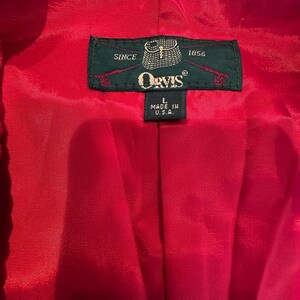 Puede incluir: Primer plano del interior de una prenda roja con una etiqueta verde. La etiqueta dice "Orvis" e incluye el texto "Since 1856" y "Made in U.S.A.". La prenda es de un rojo s&oacute;lido y vibrante.
