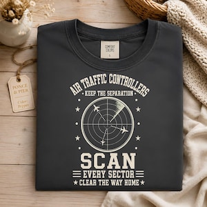 May include: A dark gray crew neck t-shirt featuring a white graphic of an air traffic control radar screen with three airplanes. The text reads: AIR TRAFFIC CONTROLLERS KEEP THE SEPARATION SCAN EVERY SECTOR CLEAR THE WAY HOME. Size L label is visible.