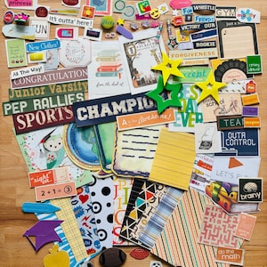 May include: A collection of assorted paper stickers and die-cut ephemera featuring various themes including sports, school, animals, and motivational phrases like Champion, Forgiveness, and A is for Awesome, alongside geometric and striped patterns.