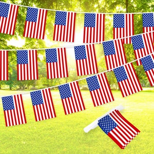 May include: A string of red, white, and blue American flag pennants hanging against a green, leafy background. The pennants are strung together with white string and are all the same size.