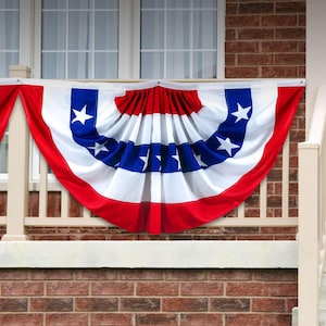 May include: Red, white, and blue pleated fabric bunting with stars, hanging from a white railing on a brick house.
