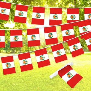 May include: A red, white, and green Peruvian flag bunting with the Peruvian coat of arms on each flag. The bunting is strung up outdoors against a backdrop of green trees.
