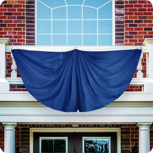 May include: A blue fabric swag banner with pleats hanging from a white railing in front of a window. The banner is a half circle shape.
