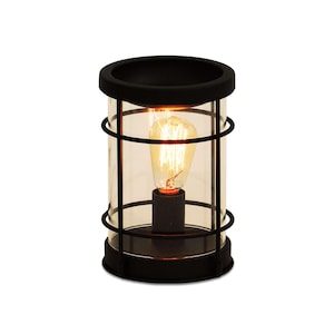 May include: A black metal and glass lantern-style lamp with a vintage Edison bulb. The lamp has a cylindrical glass shade encased in a black metal cage. The bulb is lit, emitting a warm, orange glow. The lamp is designed for indoor use.
