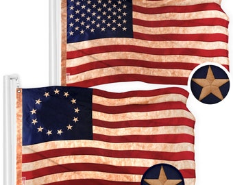 Può includere: Due bandiere americane, una con 13 stelle e l'altra con 50 stelle, entrambe con un aspetto usurato e vintage. Le bandiere sono esposte su pali bianchi su uno sfondo bianco. Ogni bandiera ha una toppa a stella blu.