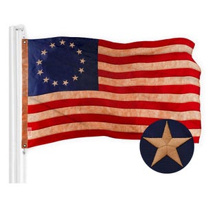 May include: A vintage-looking American flag with 13 red and white stripes and a blue canton featuring 13 white stars in a circle. The flag is waving in the wind and has a faded, distressed look. A blue star with a gold outline is in the lower right corner.