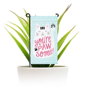 May include: A white cat with pink accents on a blue and white polka dot background. The cat is saying "You're paw some!" in pink letters. The image is a garden flag.