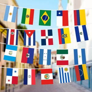 May include: A string of flags representing different countries, including the United States, Canada, Mexico, Brazil, Argentina, and others. The flags are hanging from a string against a blurred background of a city street.