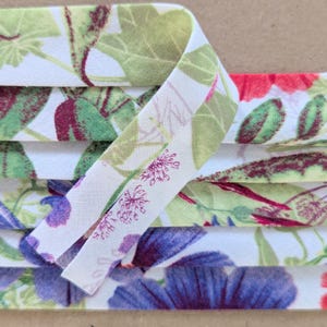 May include: A close-up of a white fabric with a floral print. The fabric is folded in layers, and the print features green leaves, purple flowers, and red flowers.