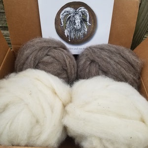 May include: A cardboard box filled with four balls of wool. Two balls are white and two are brown. The box has a book on top that says "The Shepherd's Rug, A Braided Wool Rug from Roving".
