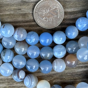 May include: A strand of blue agate beads, each bead is approximately the size of a US quarter. The beads have a light blue color with white and brown stripes.