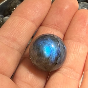 May include: A dark blue labradorite sphere with iridescent blue and green flashes. The sphere is smooth and polished.