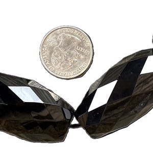 May include: A strand of black faceted gemstone beads. The beads are large and have a geometric shape. A US quarter is included for scale.