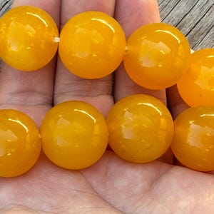 May include: A strand of smooth, round, vibrant yellow beads. Each bead features a polished, glossy finish that reflects light, creating a bright and uniform appearance across the entire string of spherical components arranged in a linear sequence.