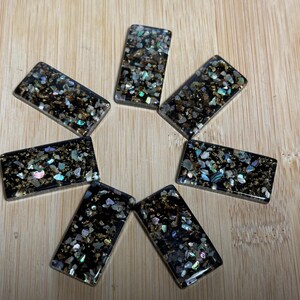 May include: Seven rectangular black resin tiles with gold and iridescent glitter embedded in the resin.