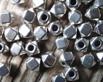 May include: A close-up of a pile of silver-toned metal beads. The beads are shaped like a five-pointed star with a hole in the center. The beads are scattered on a wooden surface.