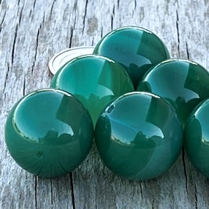 May include: A collection of six polished, emerald green spheres. The spheres are arranged closely together, reflecting light and the surrounding environment. The objects are on a weathered, light-colored wooden surface.