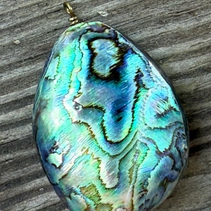 May include: A teardrop-shaped pendant with iridescent blues, greens, and purples. The abalone shell pendant has a swirling pattern and a gold-colored bail for attaching to a chain. The natural shell has a polished finish.